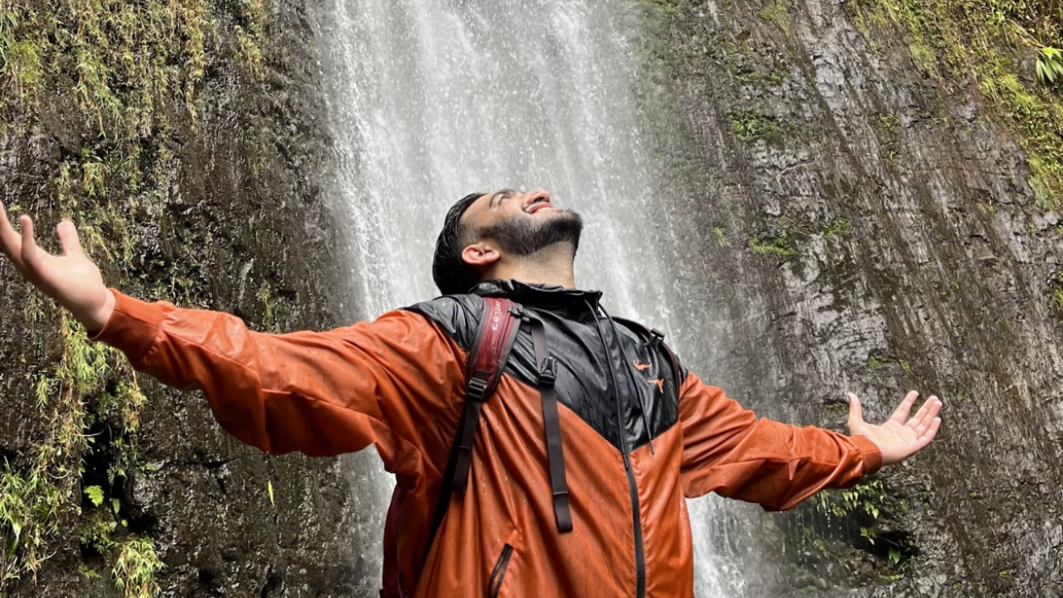 Dr. Tatapudi standing with his arms outstretched in front of a waterfall
