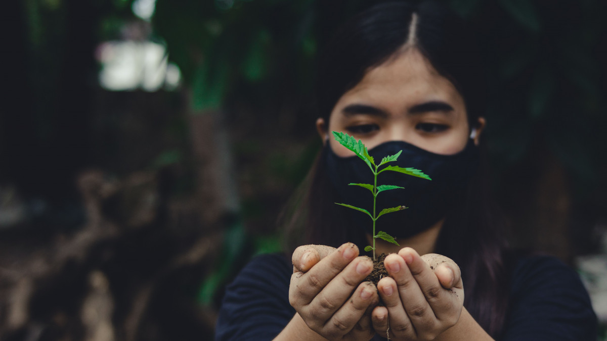 climate and health - woman holding plant while wearing face mask
